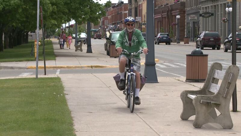 Man biking and people walking through downtown Menominee. (WLUC photo)